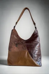 Cartera de cuero combinada con texturas y pelo natural con estampado animal print tipo vaca, diseño envolvente con líneas orgánicas, asa de hombro y bolsillos exteriores.