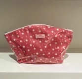 Neceser transparente con estampado de estrellas blancas sobre fondo rosado.