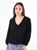 Camisa negra de manga larga con cuello redondo y cierre frontal de botones. La tela parece tener textura y las mangas son abullonadas con puños ajustados.