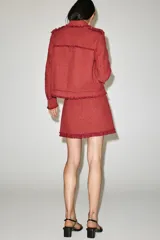 Minifalda de tiro medio confeccionada en tejido de tweed rojo, con diseño estructurado y terminaciones deshilachadas en el borde inferior. Cuenta con cierre en la espalda con cremallera oculta en costura.