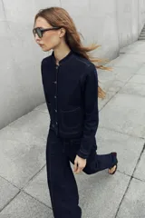 Chaqueta de jean azul oscuro, con cuello mao, cierre frontal de botones metálicos y dos bolsillos frontales de parche.