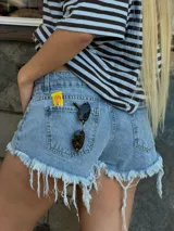 Short de jean de tiro medio, color celeste con efecto lavado, diseño corto de corte ajustado y ruedos deshilachados con flecos pronunciados. Cuenta con bolsillos clásicos y detalles de roturas sutiles en el frente.