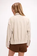 Campera de gamuza color beige con diseño de calados florales en hombros y espalda, cierre frontal y cuello camisero. Presenta un corte relajado y textura suave.