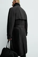 Trench de corte regular confeccionado en tejido técnico italiano repelente al agua. Presenta cuello con solapas de muesca, cierre frontal de botonadura cruzada, cinturón ajustable del mismo tejido, bolsillos de vivo en la cadera, manga larga con puños ajustables y abertura central en la espalda.