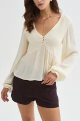 Blusa blanca de viscosa, con cuello en V, detalles de frunces en el frente, botones decorativos y mangas largas holgadas.