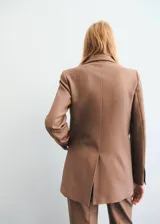 Chaqueta de traje color tostado con cuello de solapa, cierre frontal de dos botones, mangas largas y bolsillos de parche delanteros. Cuenta con forro interior y diseño recto.
