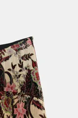 Falda de tiro alto con estampado floral en tonos beige, negro y rosado. Presenta detalles de hilo metalizado vertical y bajo asimétrico con volantes.