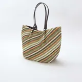 Bolso tipo capazo grande de tejido trenzado con diseño de rayas diagonales multicolor en tonos verdes, marrones, blancos y negros. Cuenta con doble asa de hombro en cuero sintético marrón.