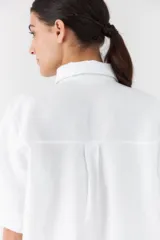 Camisa blanca de manga corta y corte recto, con cuello camisero clásico y cierre frontal de botones.