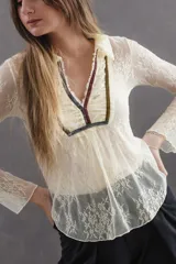 Blusa de tul bordado color manteca, con estilo romántico bohemio. Presenta cuello tipo camisa, escote en V con pechera fruncida y detalles de tiras de terciopelo en colores contrastantes. Posee mangas largas y diseño levemente elastizado.