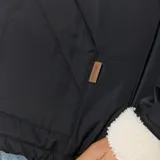 Campera bomber Rip Curl color negro, con cierre frontal, capucha y puños con forro de corderito sintético color crema. Presenta un diseño con cordón ajustable en la cintura.