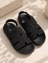 Sandalia tipo romana color negro, con múltiples tiras anchas en el empeine, suela plana y tira ajustable con cierre de velcro en el talón.