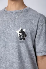Remera de algodón con efecto acid wash en color gris oscuro. Presenta un diseño estampado en el pecho con una estrella amarilla y un personaje animado, y un corte semi-oversize.