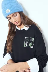 Remera de manga larga negra con cuello redondo y puños blancos visibles, presentando un estampado gráfico con motivos celestiales en el pecho.