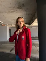 Blazer rojo con solapas, cierre con un botón dorado y escudo bordado en el bolsillo.