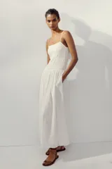 Vestido midi de color blanco con escote recto y tirantes finos ajustables. Presenta un cuerpo con tejido elástico tipo nido de abeja y detalles de flores bordadas en la parte superior. Cuenta con bolsillos laterales ocultos y forro interior.