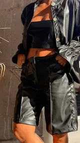 Bermuda de tiro alto confeccionada en cuerina negra, con corte recto y largo hasta la rodilla.