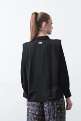 Camisa negra de estilo sastrero con cuello clásico, frente abotonado y mangas largas con puños ajustados. Presenta un diseño con hombreras sutiles que aportan estructura a la prenda.