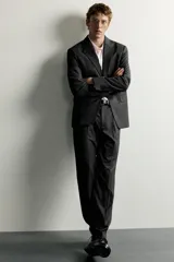 Pantalón de traje slim fit para hombre, color gris oscuro, con bolsillos frontales y bolsillos traseros de doble vivo con botón. Cuenta con cierre frontal de cremallera y botón, y presillas para cinturón.