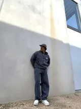 Conjunto de dos piezas compuesto por un buzo con capucha y cierre frontal y un pantalón de jogging, ambos confeccionados en tejido con efecto acid wash en color gris oscuro. El buzo cuenta con bolsillos frontales y logo bordado, mientras que el pantalón presenta un corte holgado y logo bordado en la pierna.