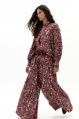 Pantalón de lino color bordó con estampado floral de margaritas en blanco, azul y naranja. Diseño de pierna ancha, tiro medio-alto con tablas delanteras, elástico en la parte trasera y bolsillos laterales.