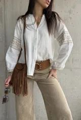 Camisa blanca de calce relajado y tejido liviano, con escote en V y delicados detalles bordados geométricos en tonos tostados en las mangas abullonadas y puños.