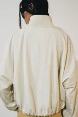 Chaqueta de nylon color crudo, con cuello alto, mangas largas, bolsillos delanteros, bajo abullonado con elástico y cierre frontal con botones forrados.