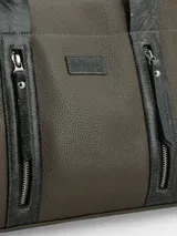 Cartera de mano color verde oliva con textura graneada, detalles en cuero gris oscuro con efecto desgastado, doble asa superior y correa larga ajustable. Presenta dos bolsillos frontales verticales con cierre metálico y placa con logo de la marca.