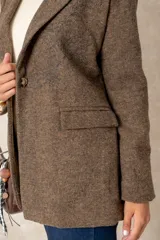 Blazer de corte sastre con diseño de espiga en tonos grises. Presenta un bordado floral lineal en el lateral, solapas clásicas, cierre frontal con un botón y bolsillos con solapa.