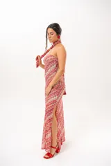Vestido largo de crochet con escote strapless y lazo integrado para el cuello, con diseño de patrón en zigzag en tonos rojos, blancos y beige, y aberturas laterales en la falda.