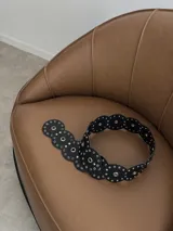 Cinturón de ecocuero negro con diseño de círculos unidos, cada uno con un ojal central grande y múltiples ojales pequeños alrededor.