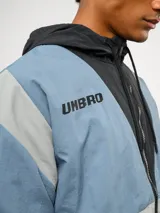 Campera de nylon Umbro con capucha, cierre frontal y diseño de bloques de color en gris, blanco y azul. Puños y dobladillo elásticos.