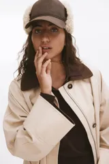 Gorra de tela con estampado a cuadros en tonos marrones y azules, con orejeras de sherpa suave que se abrochan con una trabilla ajustable en la parte superior. Forro de sherpa.