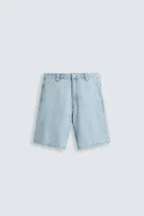 Shorts de denim de algodón, color celeste lavado, de corte regular fit y largo hasta la rodilla. Presenta cierre frontal con cremallera y botón, bolsillos delanteros y bolsillos traseros de plastrón. El borde inferior tiene un acabado deshilachado.