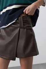 Short tipo skort de cuero sintético color marrón, con diseño envolvente y tiro medio.