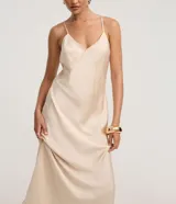 Vestido largo (midi) color beige claro, estilo slip dress, con escote en V y breteles finos ajustables. Presenta un recorte sutil en el área del busto.