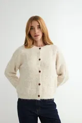 Cardigan de punto con textura suave, color beige jaspeado, de corte holgado, cuello redondo y cierre frontal con botones oscuros.