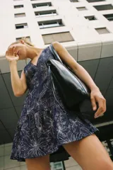 Vestido corto sin mangas de color azul marino, con escote en V y bordados florales a contraste. Presenta un diseño ajustado con corte en la cintura y falda con volante en el bajo. Cuenta con cierre de cremallera en la espalda.
