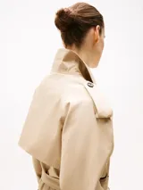 Gabardina beige de algodón con corte cropped, doble botonadura, cinturón y trabillas en los hombros.