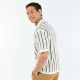 Camisa de manga corta de punto calado en color beige con rayas verticales negras, cuello tipo polo y cierre frontal con botones.