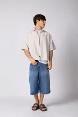 Camisa de manga corta de popelina rayada, con calce boxy y bordado sutil en el pecho. Presenta cierre frontal con botones y diseño abierto.