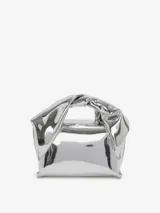 Bolso de hombro plateado con forma rectangular y efecto arrugado. Tiene asa superior con nudo y logo grabado en el frente.