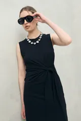 Vestido largo de punto color negro, sin mangas, con diseño entallado y un lazo lateral que permite ajustar la cintura.