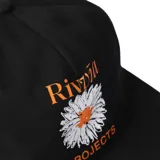 Gorra negra tipo trucker con visera plana, logo de la marca y estampa de una margarita.