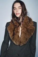 Blazer entallada de color gris oscuro, confeccionada en tejido con algodón. Presenta un cuello solapa con aplicación de pelo sintético desmontable, manga larga, bolsillos delanteros con solapa y cierre frontal con botones.