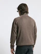 Sweater de punto color azul marino, con cuello alto, cierre frontal parcial y tapeta con botones. Presenta mangas raglán y puños y ruedo acanalados.