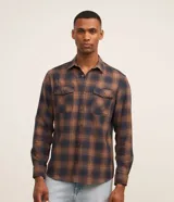 Camisa de franela a cuadros en tonos marrón y azul marino, de corte comfort con mangas largas, cuello inglés, cierre frontal con botones y dos bolsillos con solapa en el pecho.
