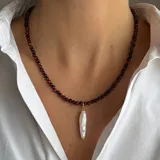 Collar compuesto por pequeñas cuentas de piedra Ojo de Buey y un dije central de perla de río natural, con cierre y detalles en baño de oro.