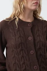 Cardigan de tejido de punto color marrón chocolate, con diseño de trenzas en el frente y mangas. Presenta cuello redondo, cierre frontal con botones al tono y puños acanalados.