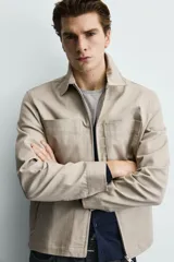 Sobrecamisa negra de corte relajado, confeccionada en tejido con mezcla de algodón elástico. Presenta cuello solapa, cierre frontal de cremallera, bolsillos de plastrón en el pecho y bolsillos de vivo en la cadera.